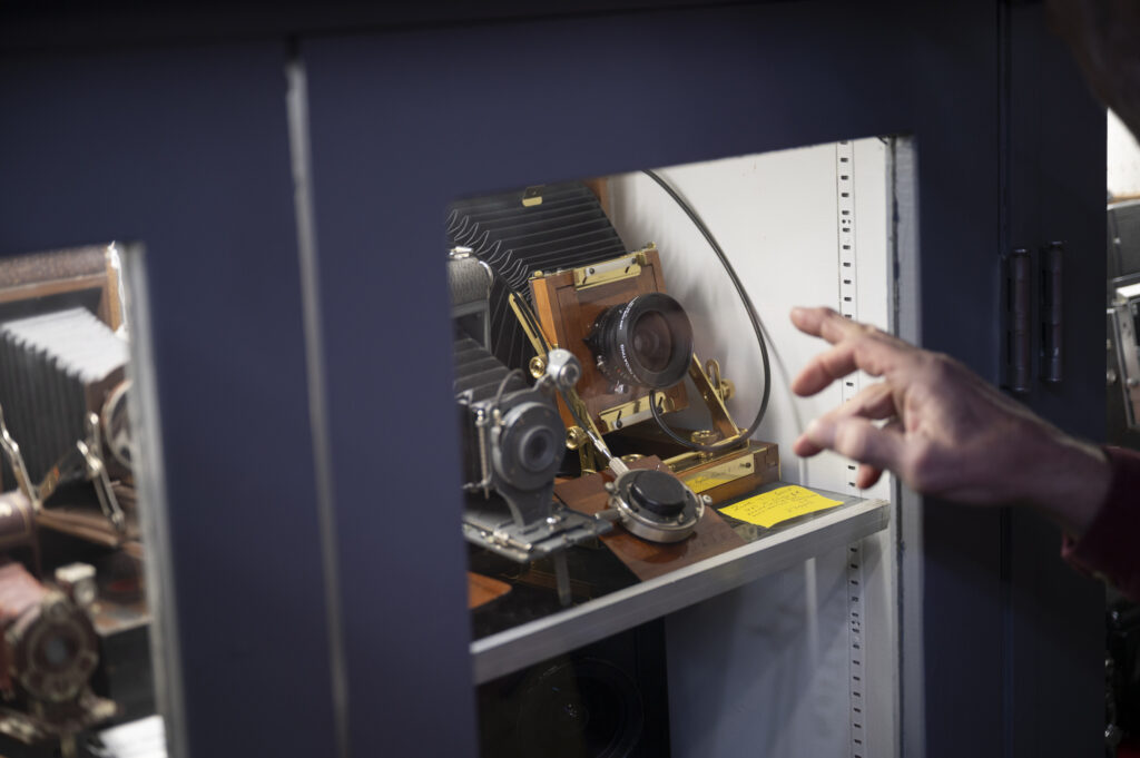 A hand points at several antique cameras made of wood and brass with paper bellows