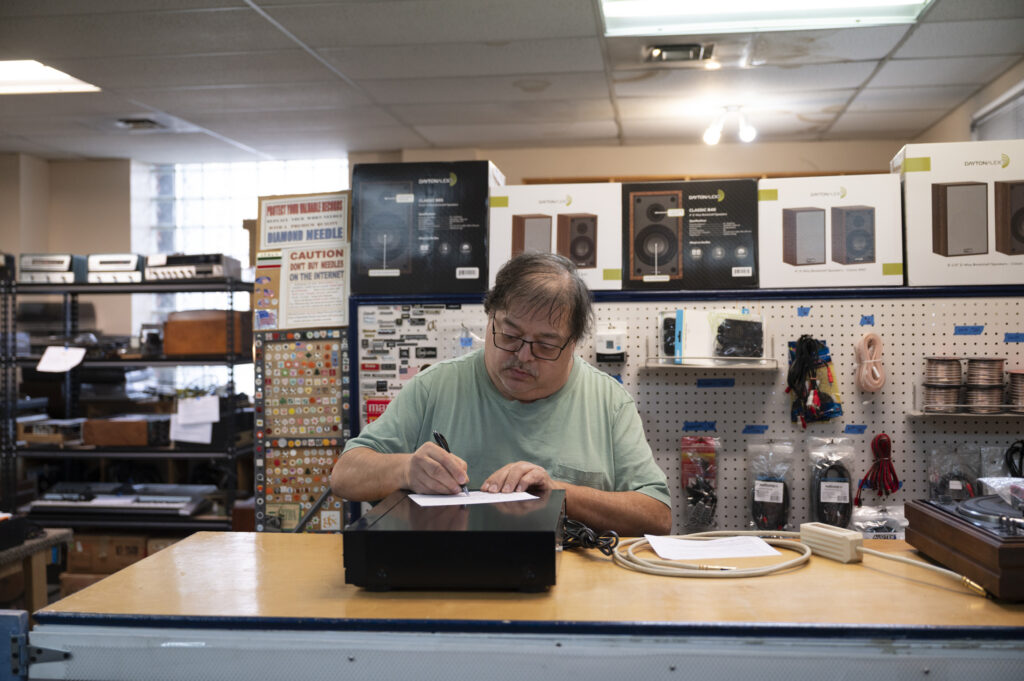A man with glasses and a mustache labels a recently repaired stereo