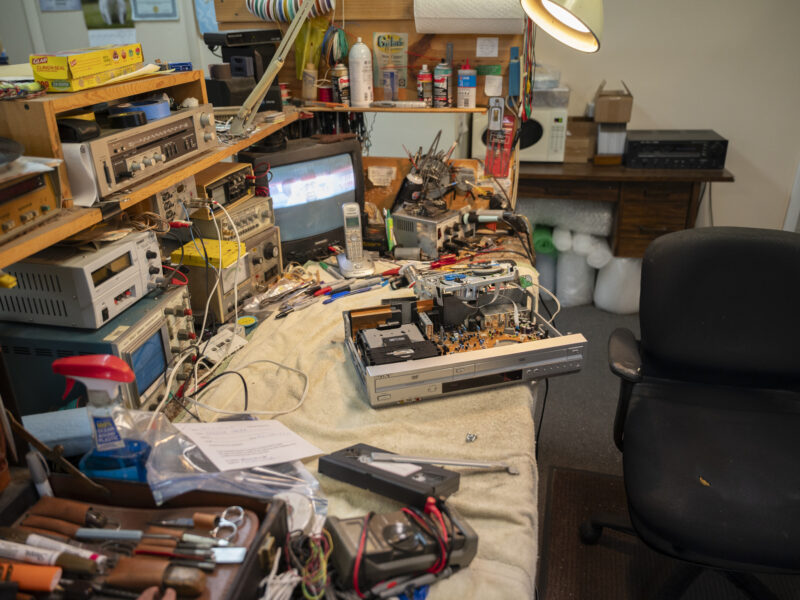 A disassembled CD/DVD player sits on a crowded workbench full of electronics parts