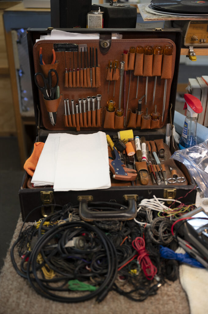An open, neatly organized leather tool kit on a crowded workbench