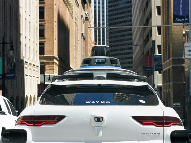 A Waymo autonomous vehicle amid 20th century skyscrapers